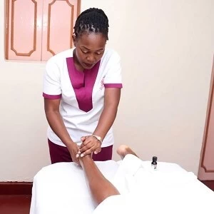 Home massage therapist from Viv's in-Houz spa, a home massage spa in Nairobi, with a client at home in Nairobi, doing a massage on the heel of the client