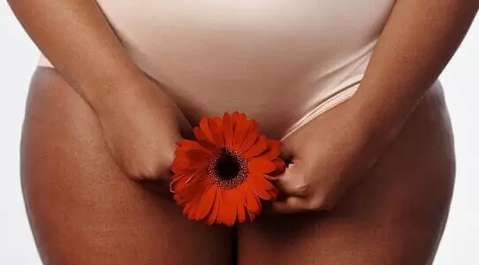 Lady holding a red flower next to her bikini area to depict vagacial