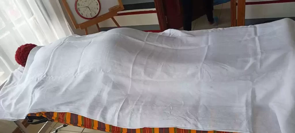 Client, a lady lying on her stomach on a massage table, covered in a towel, during a full-body massage treatment in her home in Nairobi